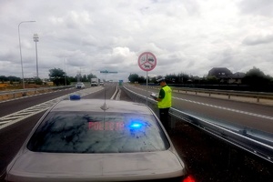 Policjant stoi przy znaku drogowym zakazującym rowerzystom poruszania się po drodze ekspresowej