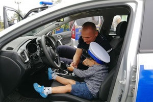 Chłopiec z czapką policjanta ruchu drogowego siedzi za kierownicą radiowozu