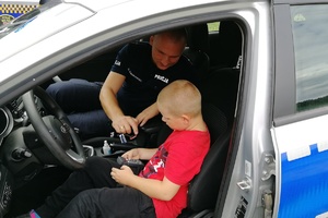 Policjant pokazuje działanie sygnalizacji radiowozu chłopcu siedzącemu w radowozie