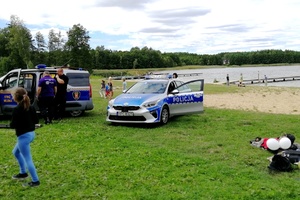Radiowóz i policjanci stojący na tle jeziora