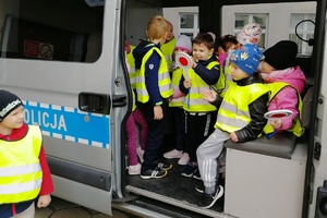 Dzieci siedzące w radiowozie pozują do zdjęcia trzymając policyjne tarcze