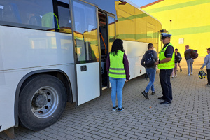 Dzieci wysiadają z autokaru, policjant rozmawia z opiekunką