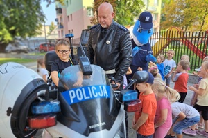 Chłopiec usiadł za kierownicą policyjnego motocykla, nadzoruje go policjant