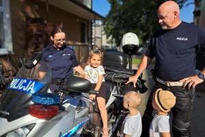 Na motocyklu siedzi dziewczynka, obok stoi policjantka i funkcjonariusz ruchu drogowego