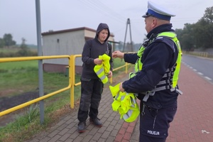 Policjant wręcza kamizelkę odblaskową chłopcu