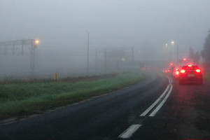 Samochody stoją we mgle przy przejeździe kolejowym