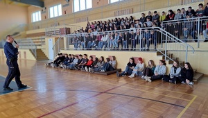 Mundurowy rozmawia z uczniami siedzącymi na widowni