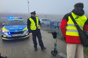 Kierujący hulajnogą z ubraną kamizelka odblaskową rozmawia z policjantami